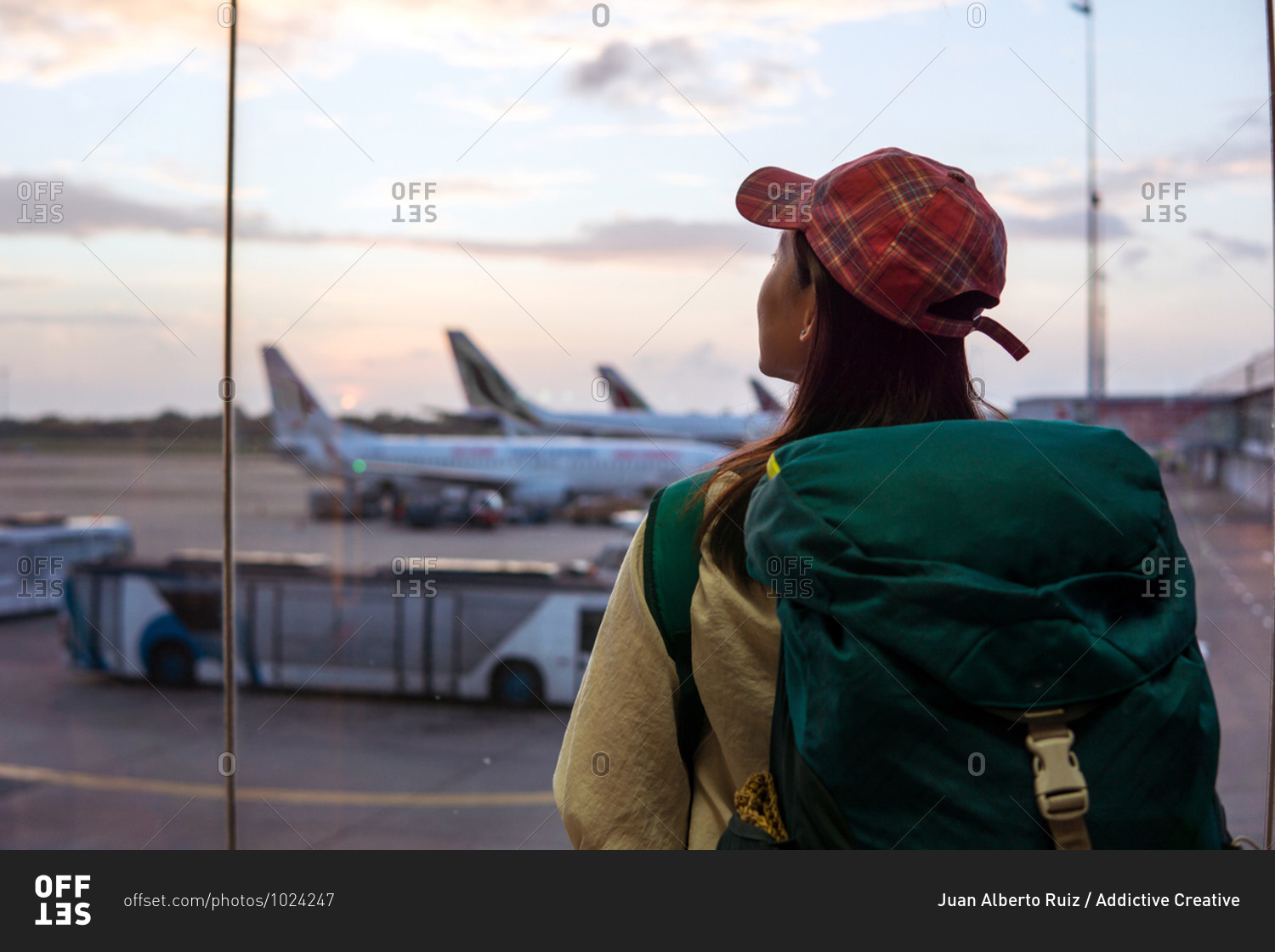 Back view of young Asian female traveler with backpack standing near window in airport terminal and observing airplanes while waiting for flight in Sri Lanka