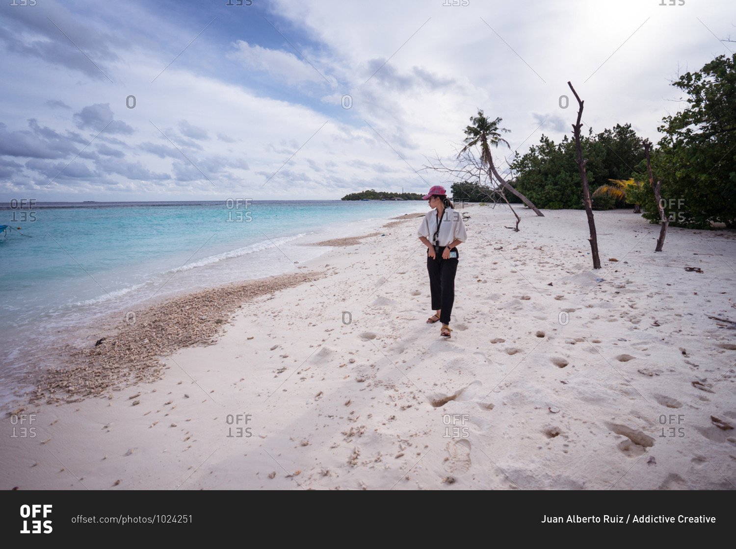 Full body front view of young Asian female traveler walking on tropical beach with white sand and blue sea water while spending summer holidays on Bodufolhudhoo island in Maldives