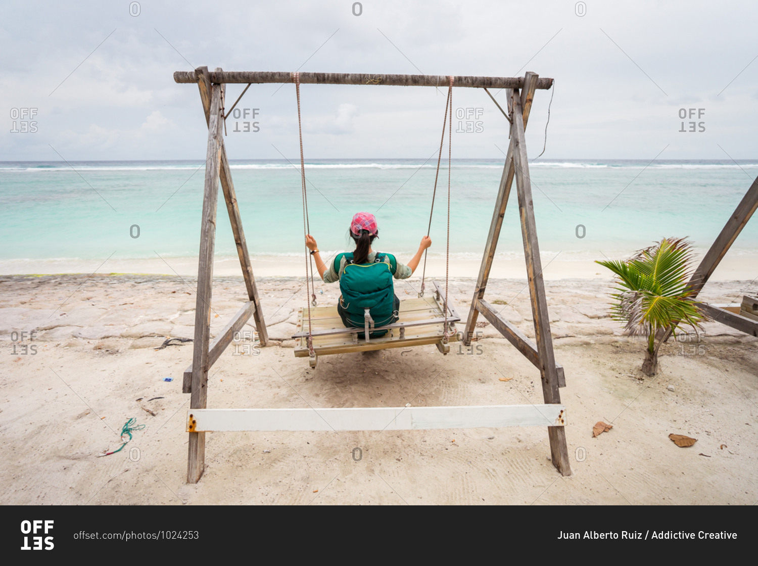 Back view of unrecognizable female traveler sitting on swings and enjoying fresh breeze while resting during summer holidays on sandy beach of Hulumale island in Maldives