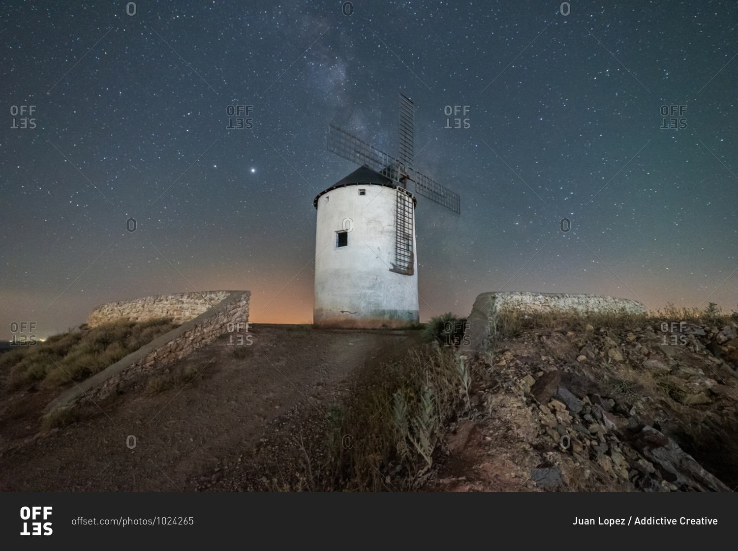 Low angle of old white windmill tower located on hill against starry night sky with Milky Way