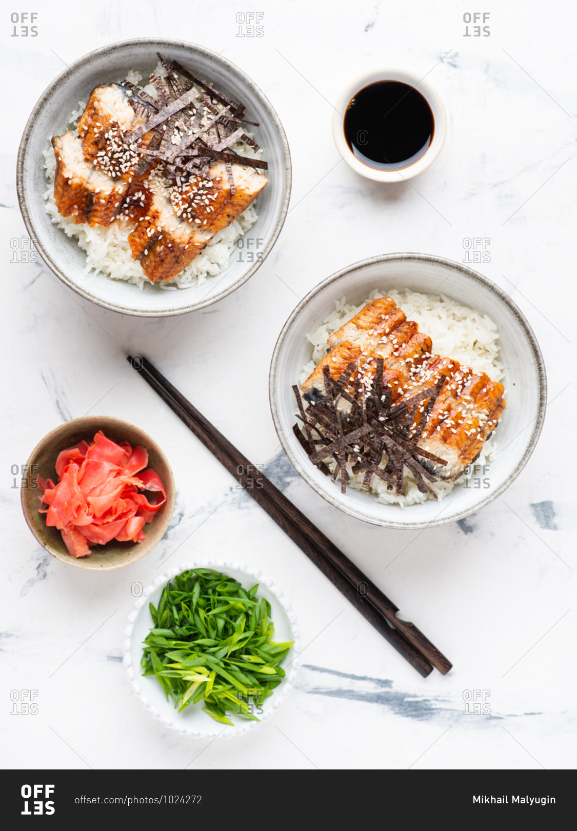 Eel with rice served in ceramic bowls with soy sauce over white background