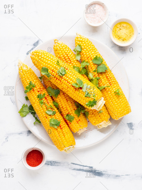 Boiled corn on cob with fresh chopped cilantro and sweet paprika powder served on ceramic plate