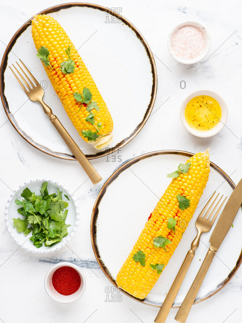 Boiled corn on cob with fresh chopped cilantro and sweet paprika powder served on ceramic plates