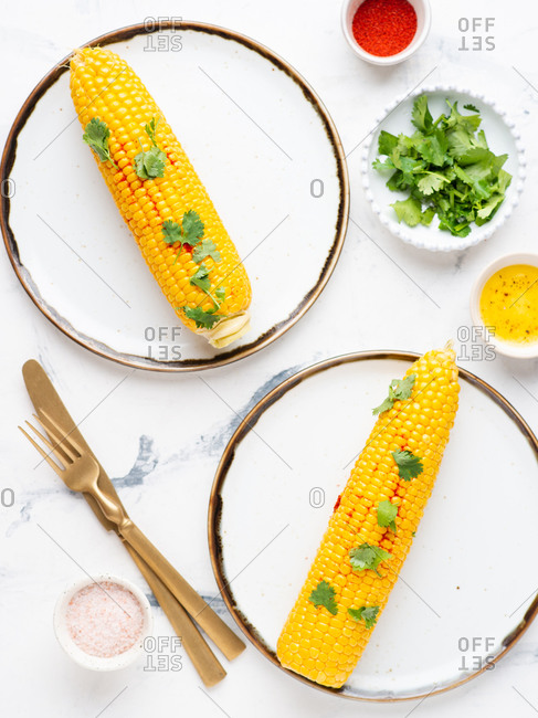 Boiled corn on cob with fresh chopped cilantro and sweet paprika powder served on ceramic plates