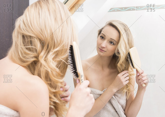Mirror reflection of a single attractive young blond woman holding and brushing hair