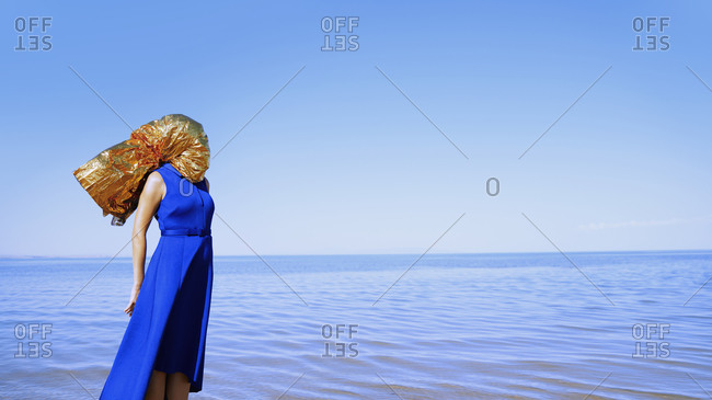 Woman with head wrapped in the golden foil standing at the sea