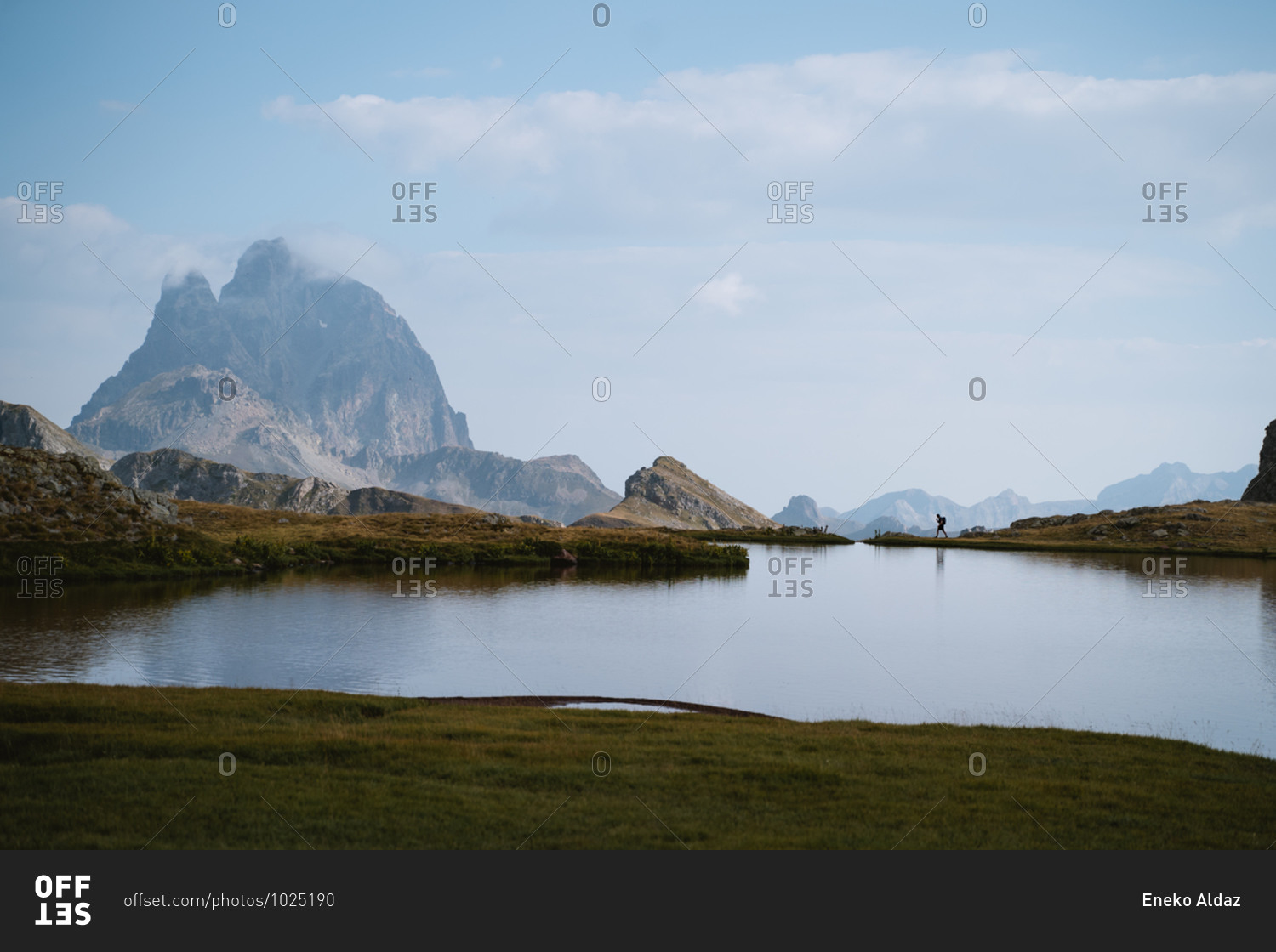 Hiker walking along the shore of an alpine lake in Pyrenees
