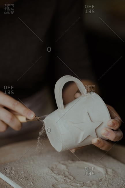 Hands of woman using tool to add detail to freshly crafted mug