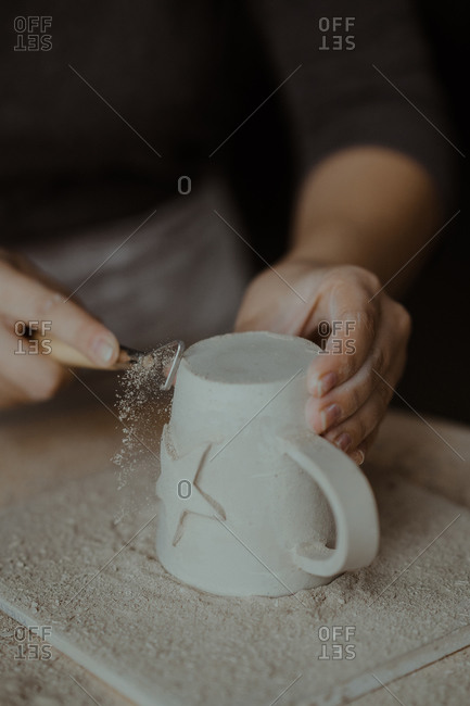 Woman using tool to add detail to freshly crafted mug