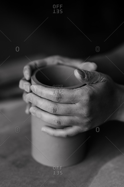 Black and white image of woman's hands shaping clay into a cylinder