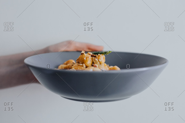 Woman holding a bowl of freshly cooked gnocchi in a creamy butter and sage sauce with crushed hazelnuts and grated parmesan cheese