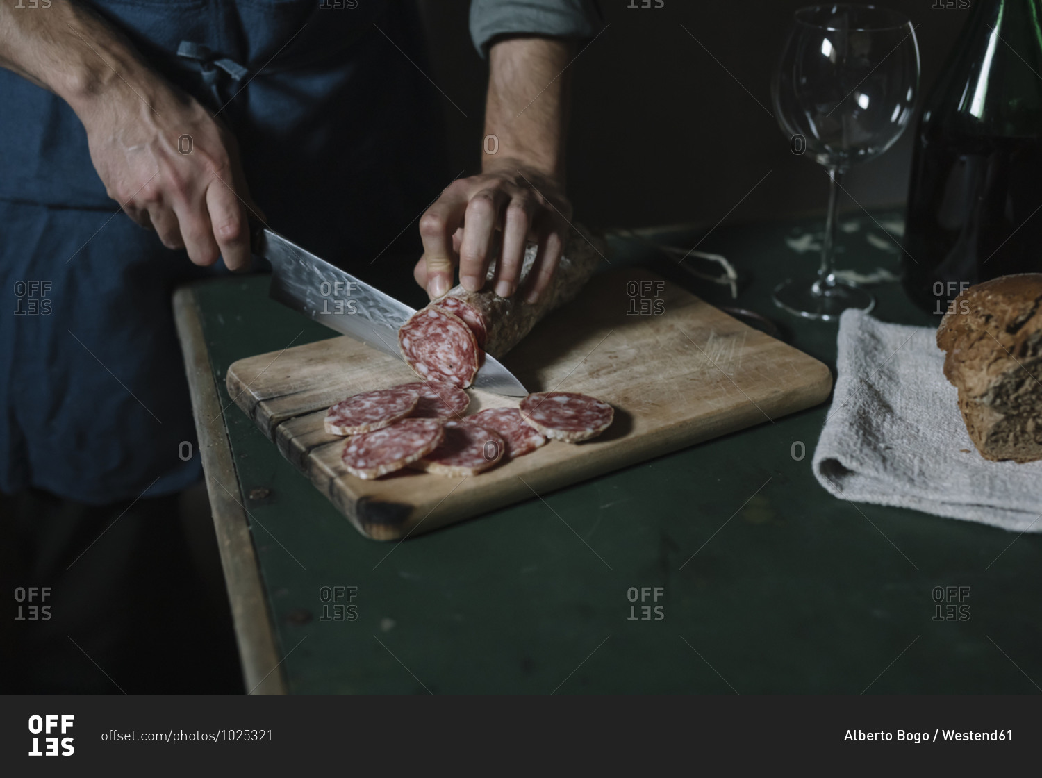 Hands of man cutting salami slices on board at table