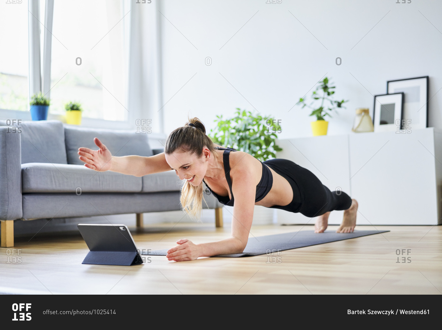 Woman extending arm during plank pose while learning exercise on internet through tablet PC