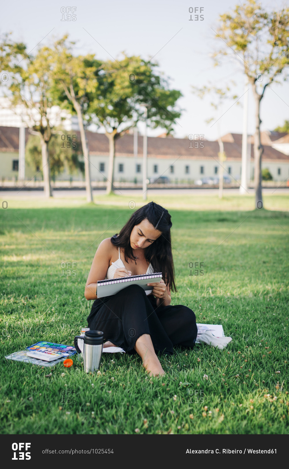 Young woman painting with watercolor in book while sitting in public park