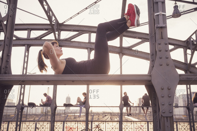Woman exercising on metal bridge in city at sunset