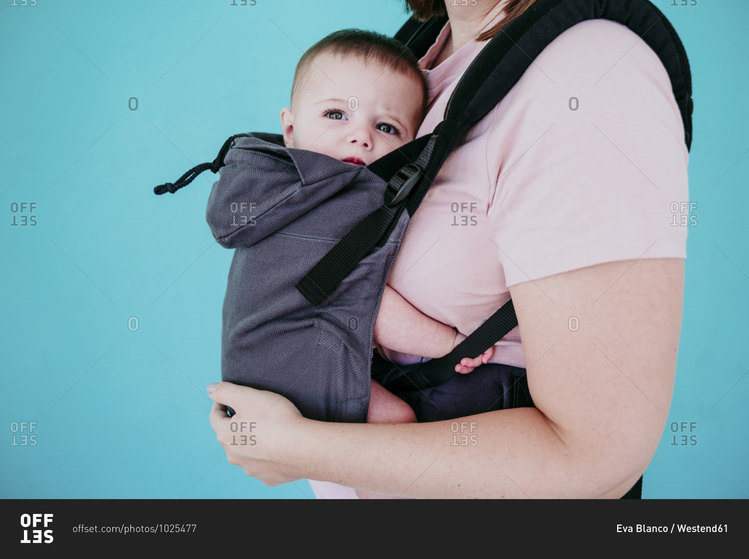 Mother and baby girl in baby carrier in front of turquoise wall