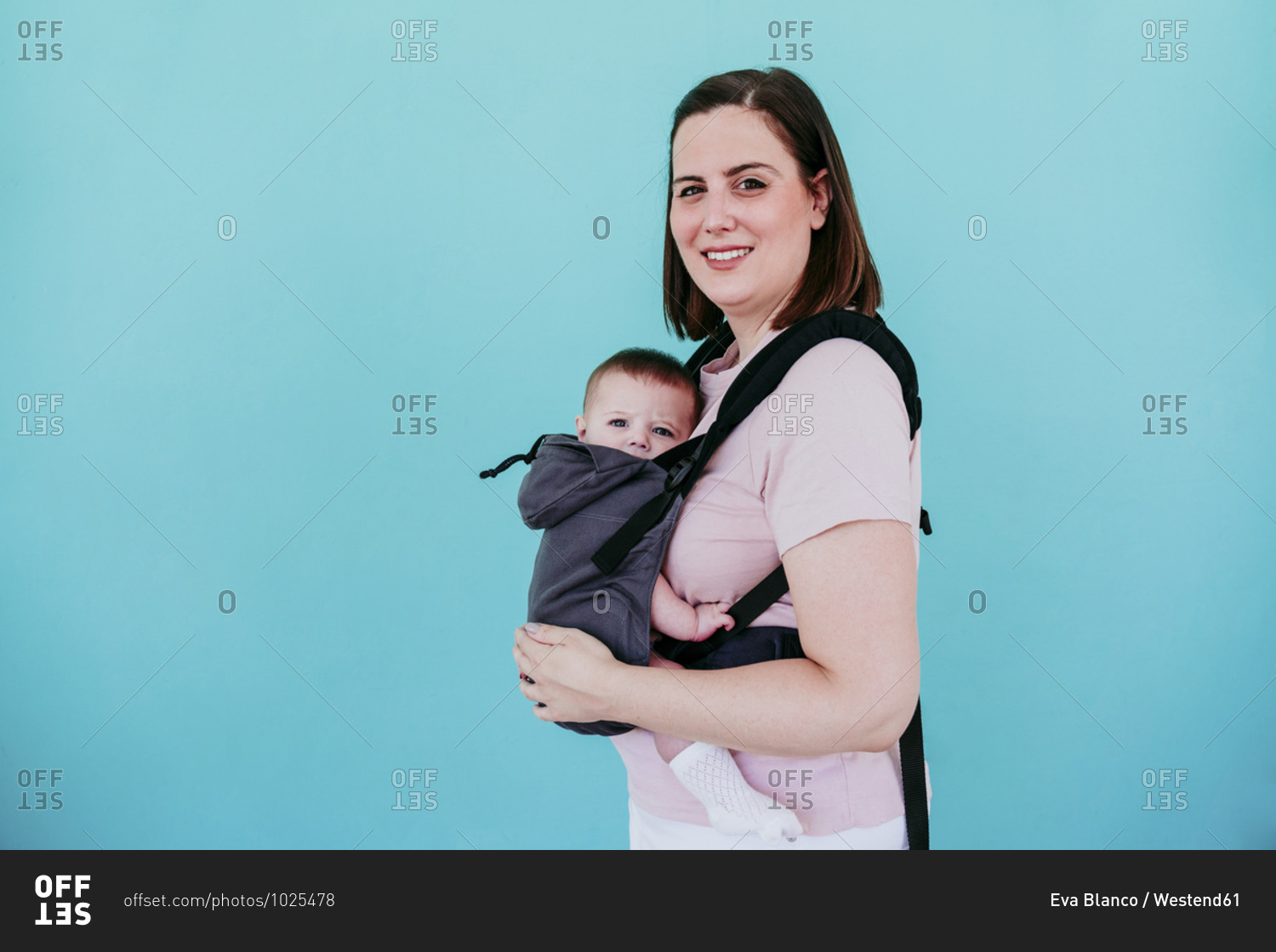 Mother and baby girl in baby carrier in front of turquoise wall