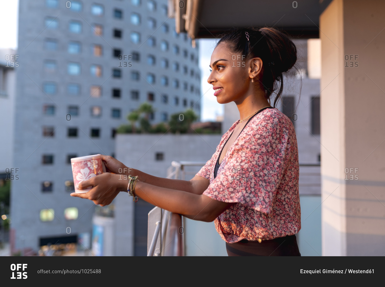 Beautiful woman holding coffee cup while standing in balcony enjoying sunset