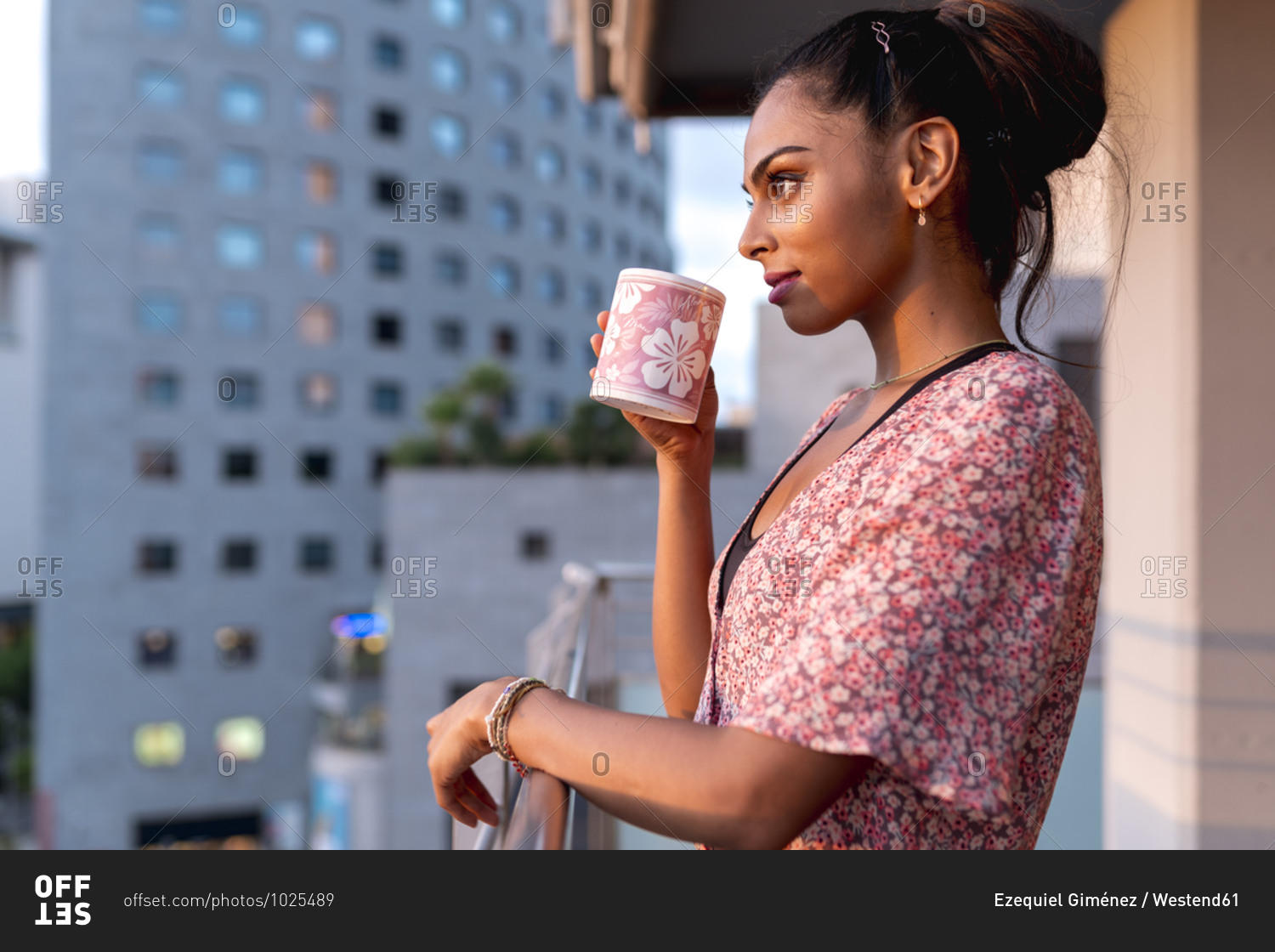 Beautiful woman standing in balcony while sipping coffee during sunset