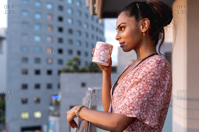 Beautiful woman standing in balcony while sipping coffee during sunset