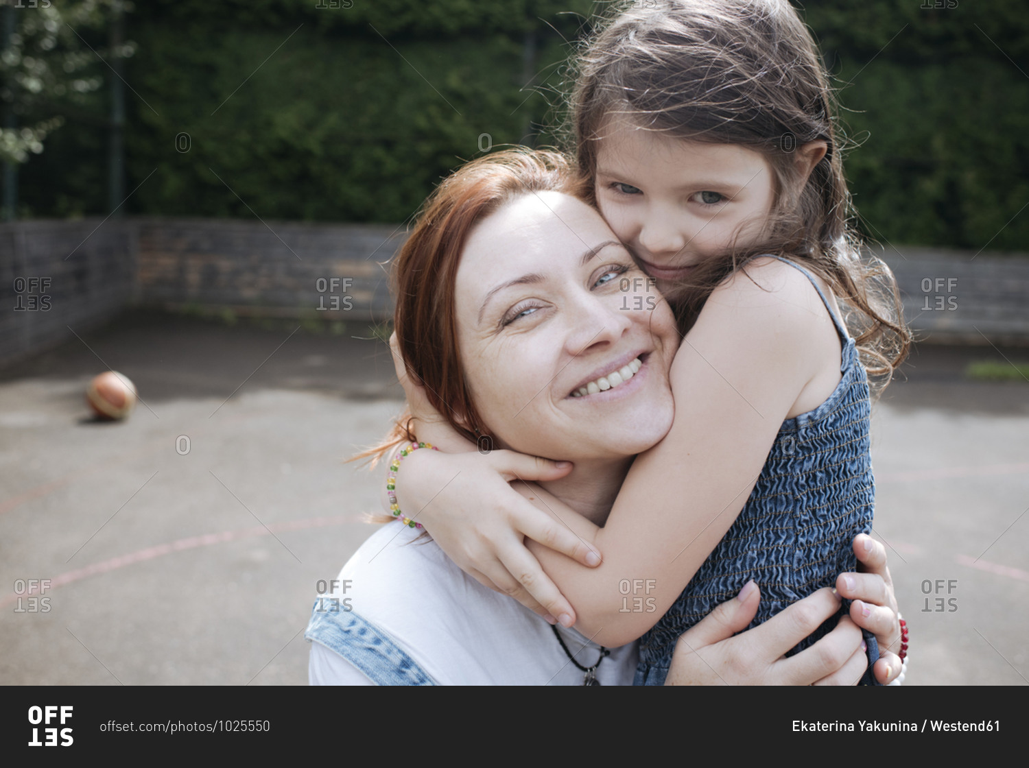 Girl embracing smiling mother at basketball court in back yard