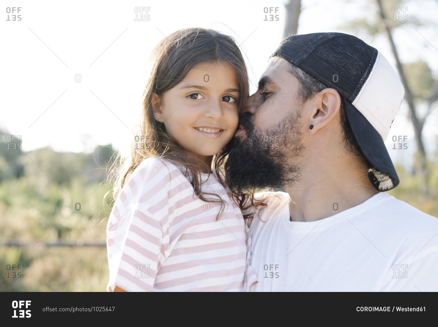 Mature man kissing cute daughter at park during sunset