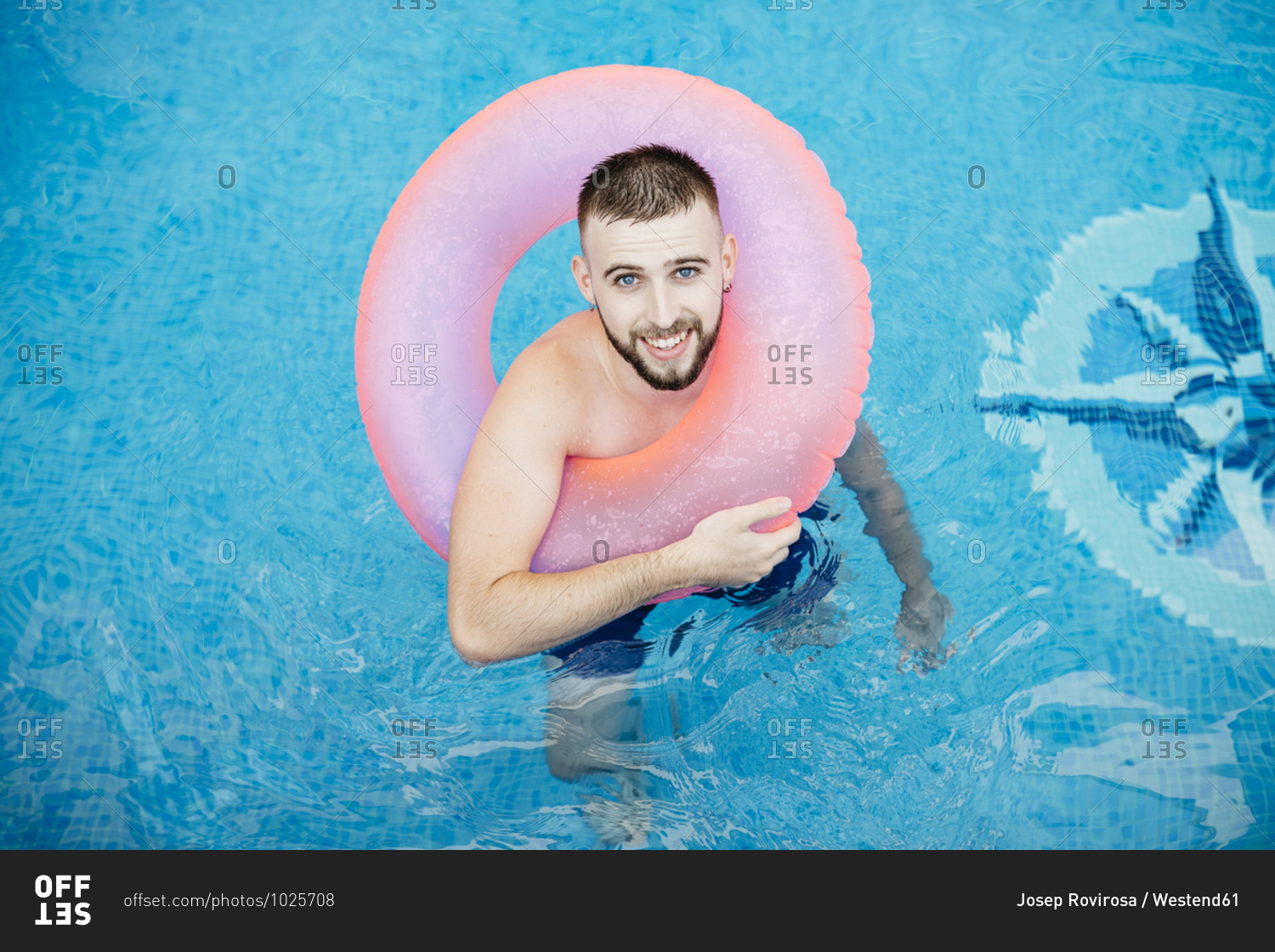 Young smiling man with pink floating tire in pool