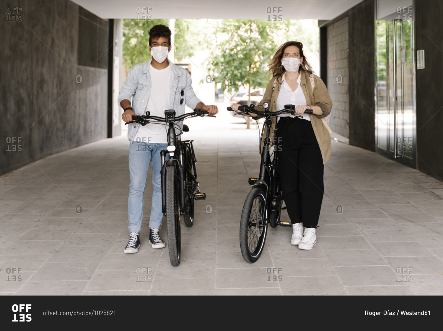 Couple in protective face masks standing with electric bicycles on footpath