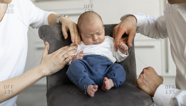 Parents sitting by baby boy sleeping on armchair at home