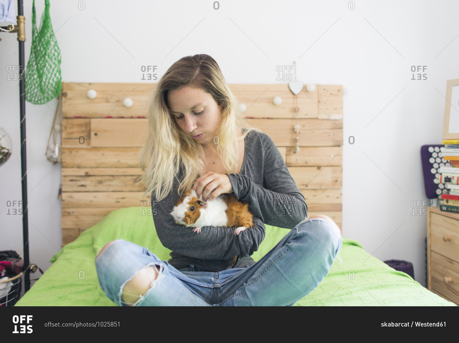 Woman holding guinea pig in arms while sitting on bed at home
