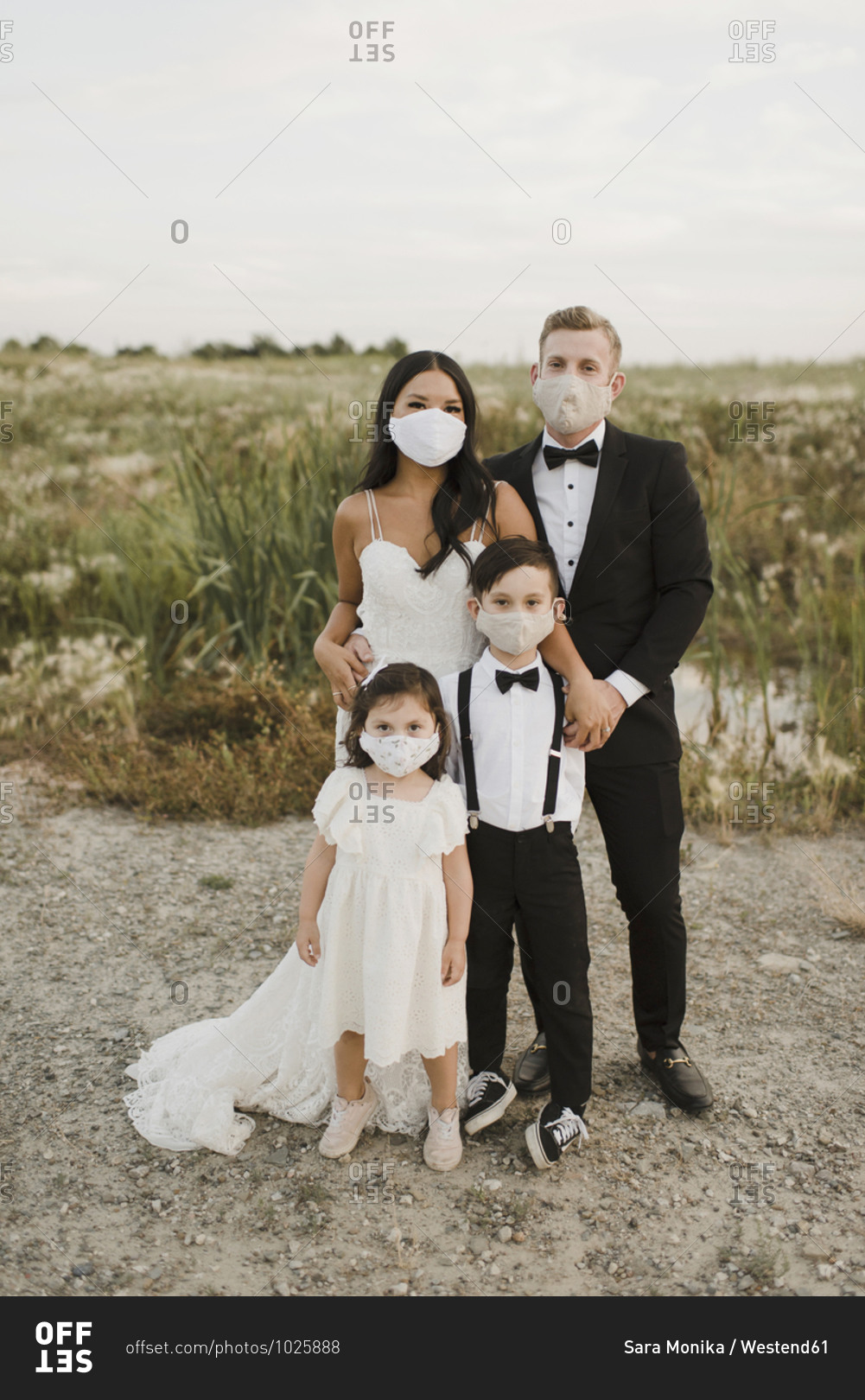 Parents and children in wedding dress wearing protective face mask while standing in field during COVID-19