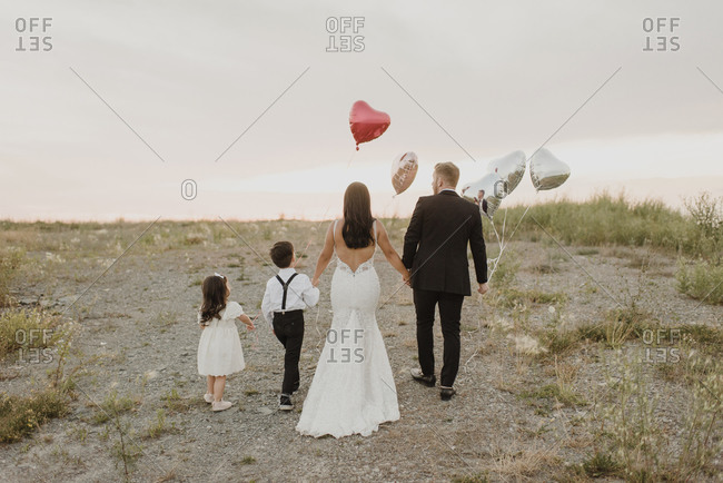 Parents and children wearing wedding dress while walking with heart shape balloons in field against sky