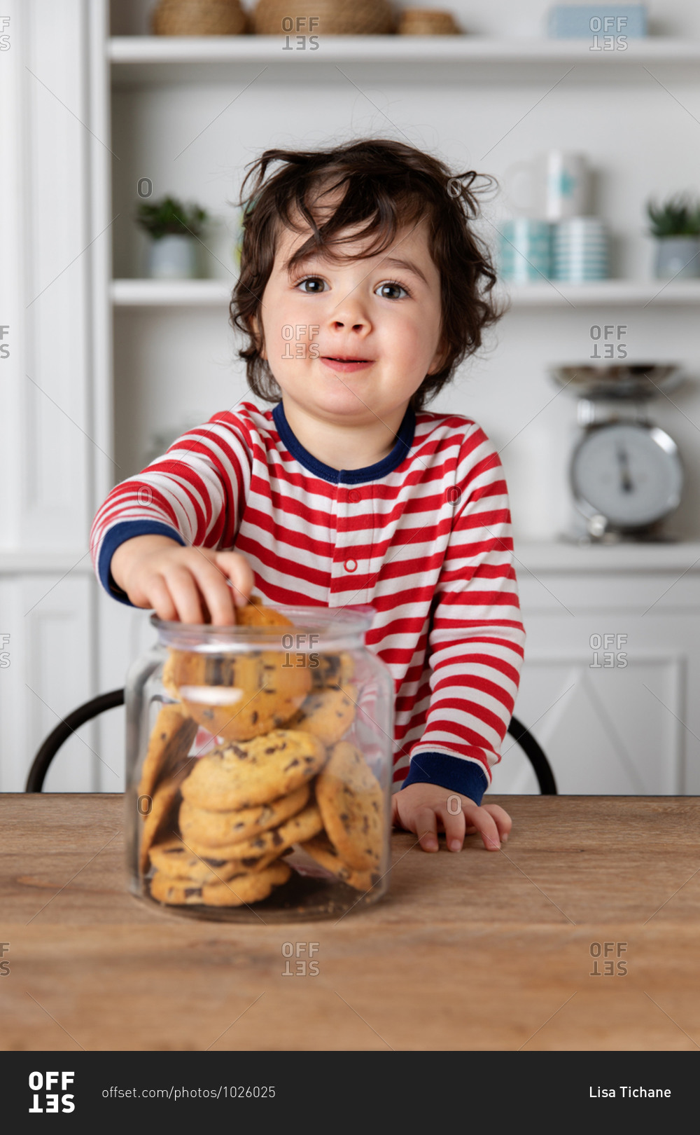 Mischievous toddler getting biscuits from cookie jar on kitchen table