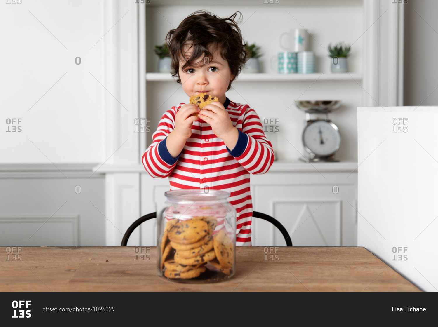 Cute little boy eating a biscuit from cookie jar at kitchen table
