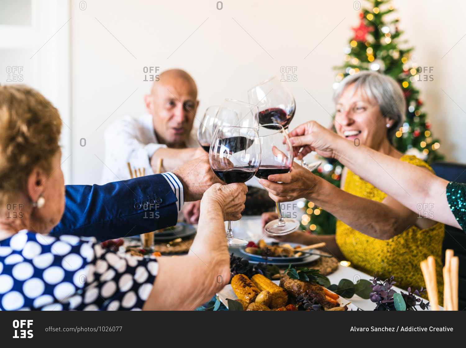 Happy partners raising glasses of alcoholic drink while gathering at table during festive event in apartment