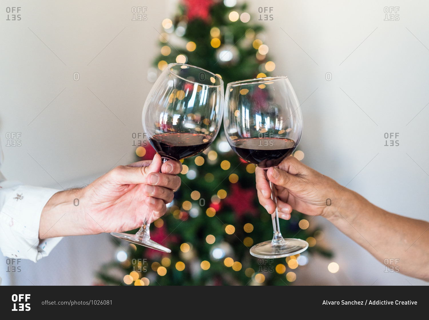 Crop unrecognizable friends with shiny glasses of alcoholic beverage near bright decorative tree during New Year holiday