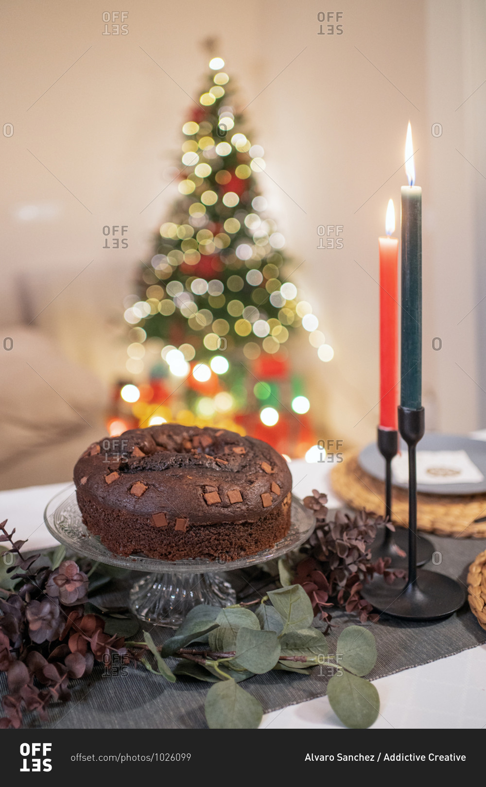 High angle of delicious chocolate cake arranged on table with candles in cozy room on background of Christmas tree with glowing garlands