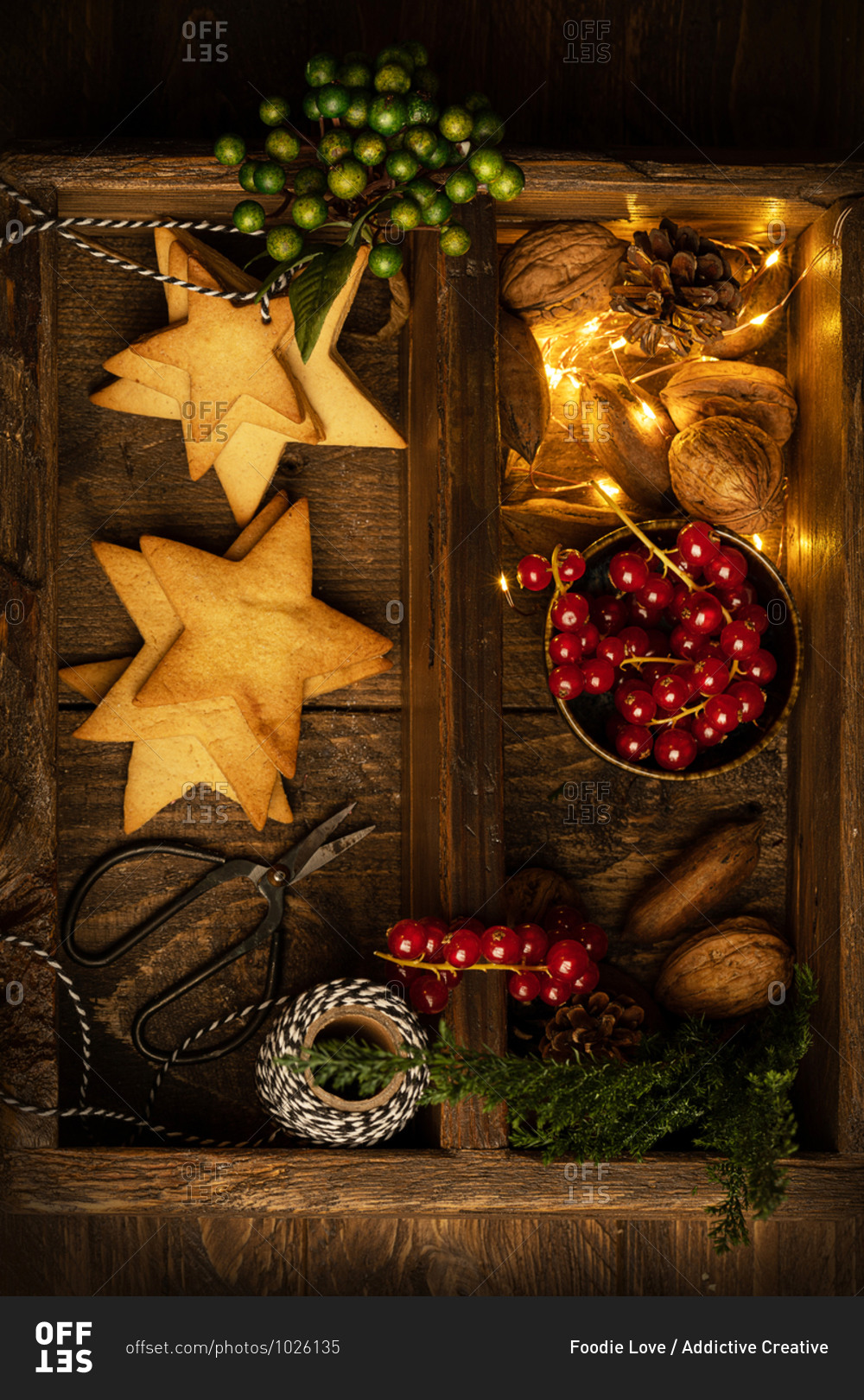 Top view of tasty cookies in shape of star and red berries arranged with illuminated garland and nuts on wooden table in dark room for Christmas celebration