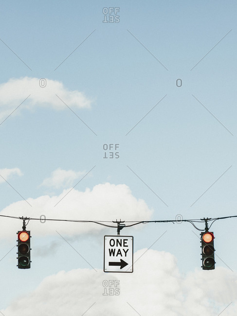 Red traffic light and one way sign below blue sky with clouds