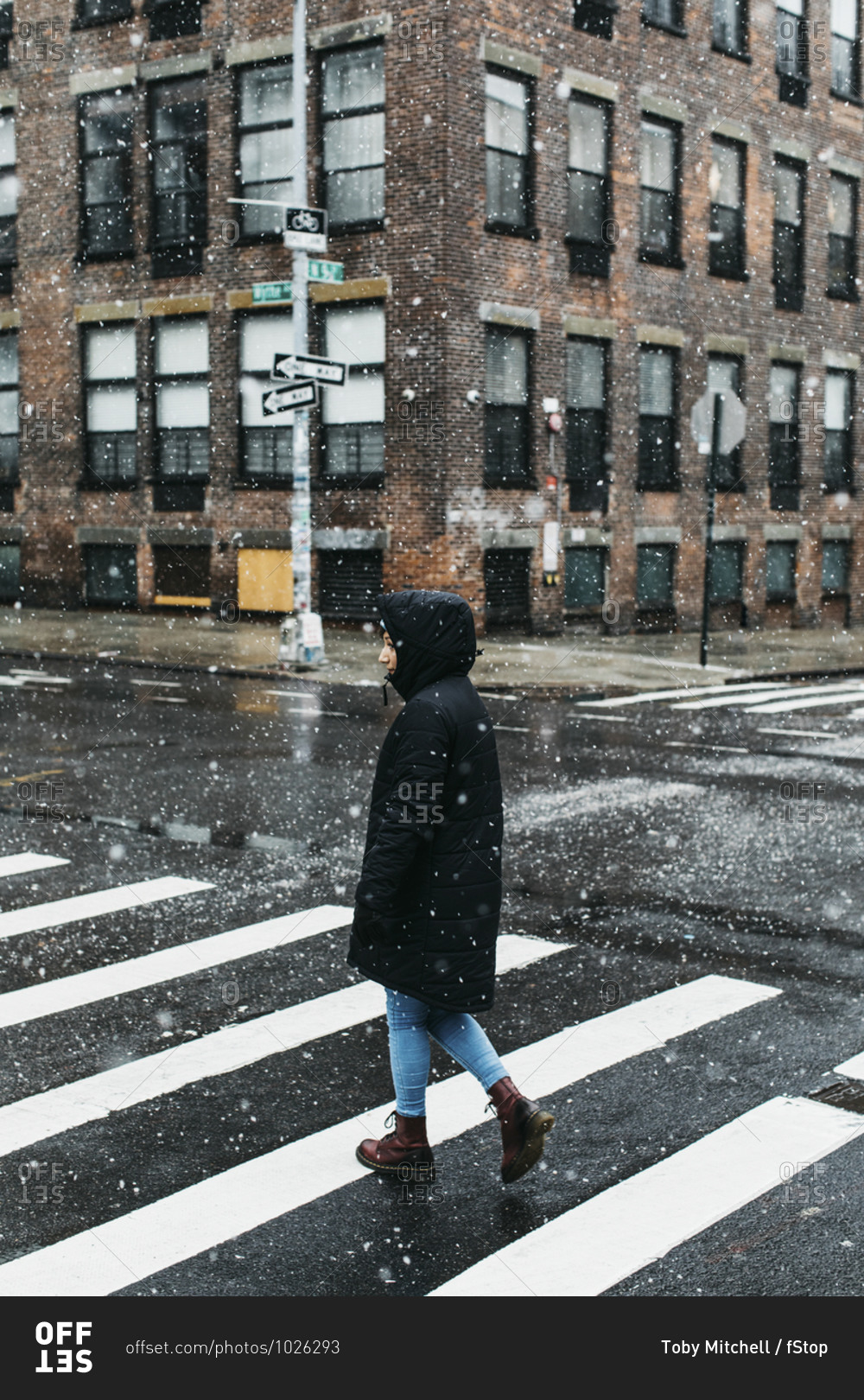 Young woman in warm jacket crossing snowy urban street, New York City, New York, USA