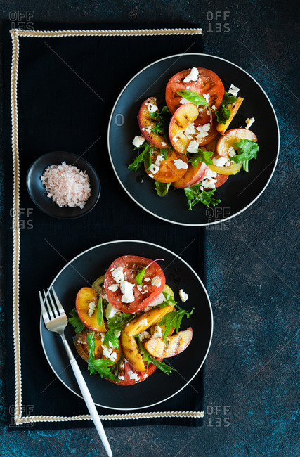 Healthy grilled peaches and tomato salad with feta cheese and green mix served for two top view