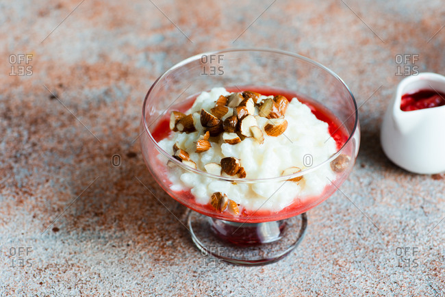Rice pudding dessert with berry sauce and nuts in glass dish