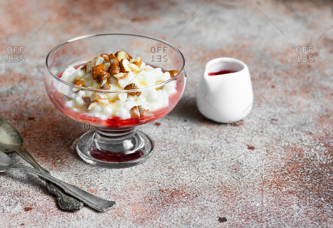 Close up of a rice pudding dessert with berry sauce and nuts in glass dish