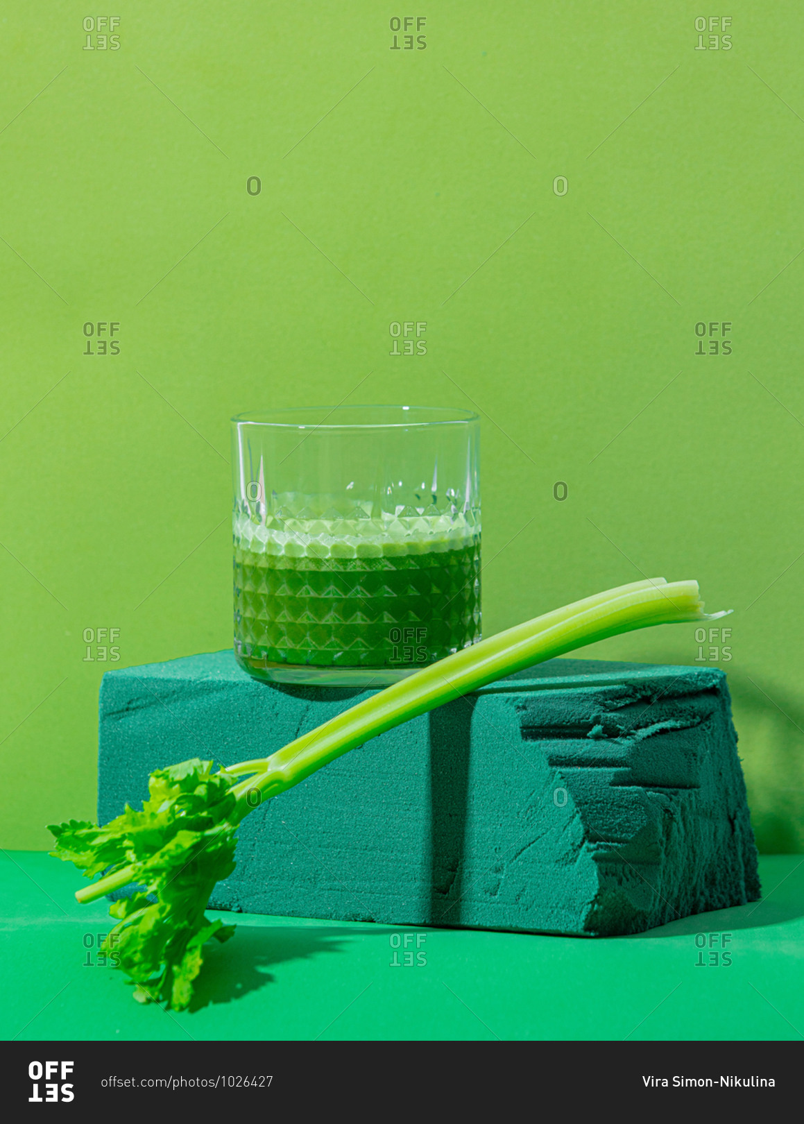 Celery stick and juice in glass on green background
