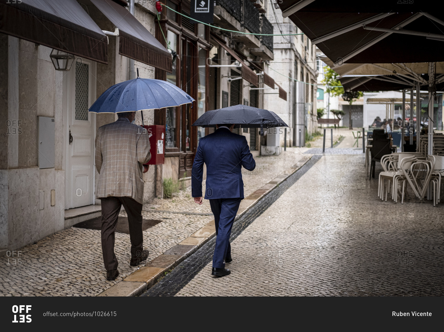 Lisbon, Portugal - June 11, 2020 : Two men in suits and carrying umbrellas walking in downtown Lisbon
