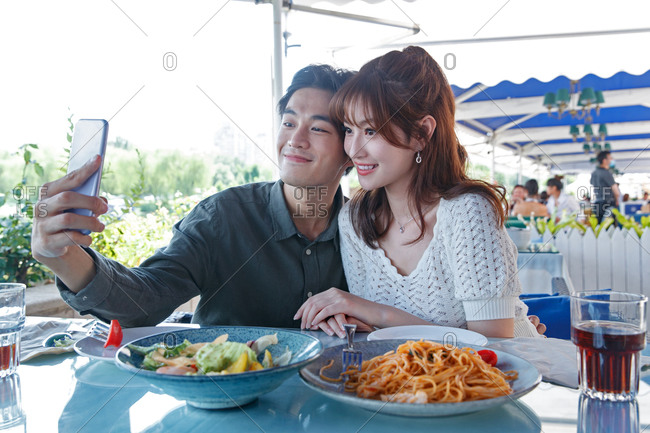 Young couple eating outdoors taking a selfie together