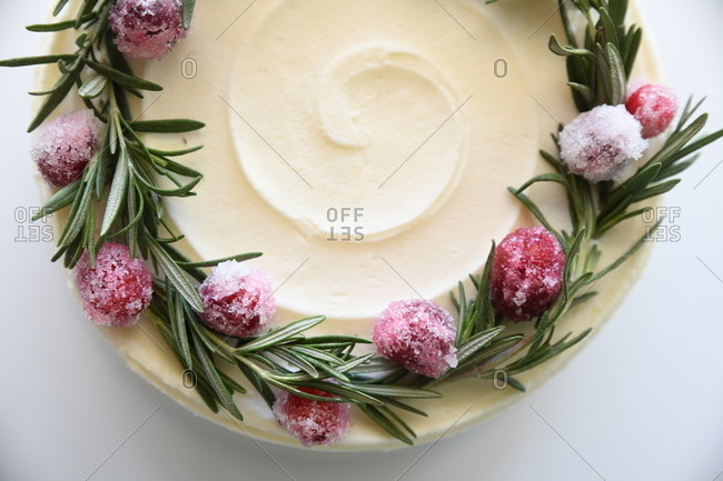 Close up of a white iced cake with rosemary and frozen fruit on white background