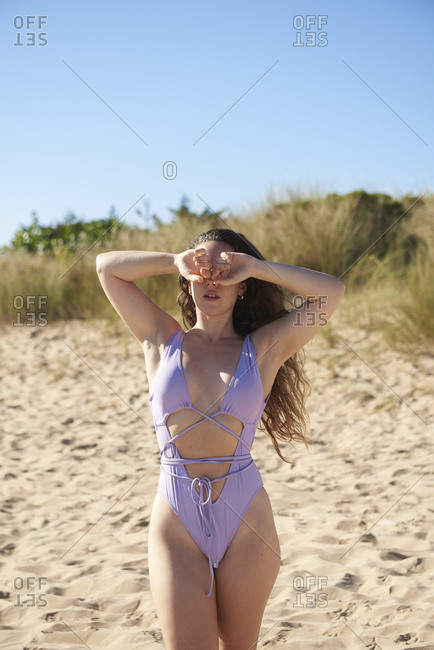 Calm female wearing swimsuit and hiding face on sandy beach enjoying sunny weather during vacation
