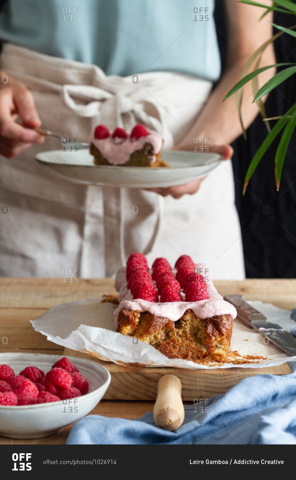 Crop anonymous female in apron standing at table with appetizing homemade cake with glaze and fresh raspberries in home kitchen
