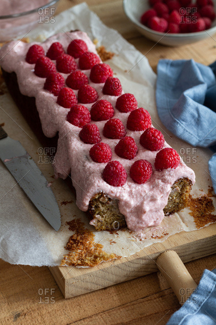 Delectable sweet homemade cake topped with whipped cream and garnished with fresh raspberries on baking paper placed on table with ingredients in kitchen